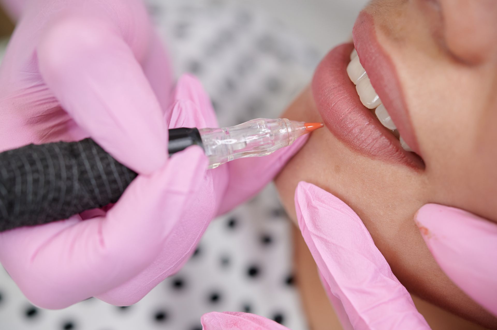 Woman with clear skin, dark hair pulled back, wearing a white tank top, smiling, and touching her face and arm.