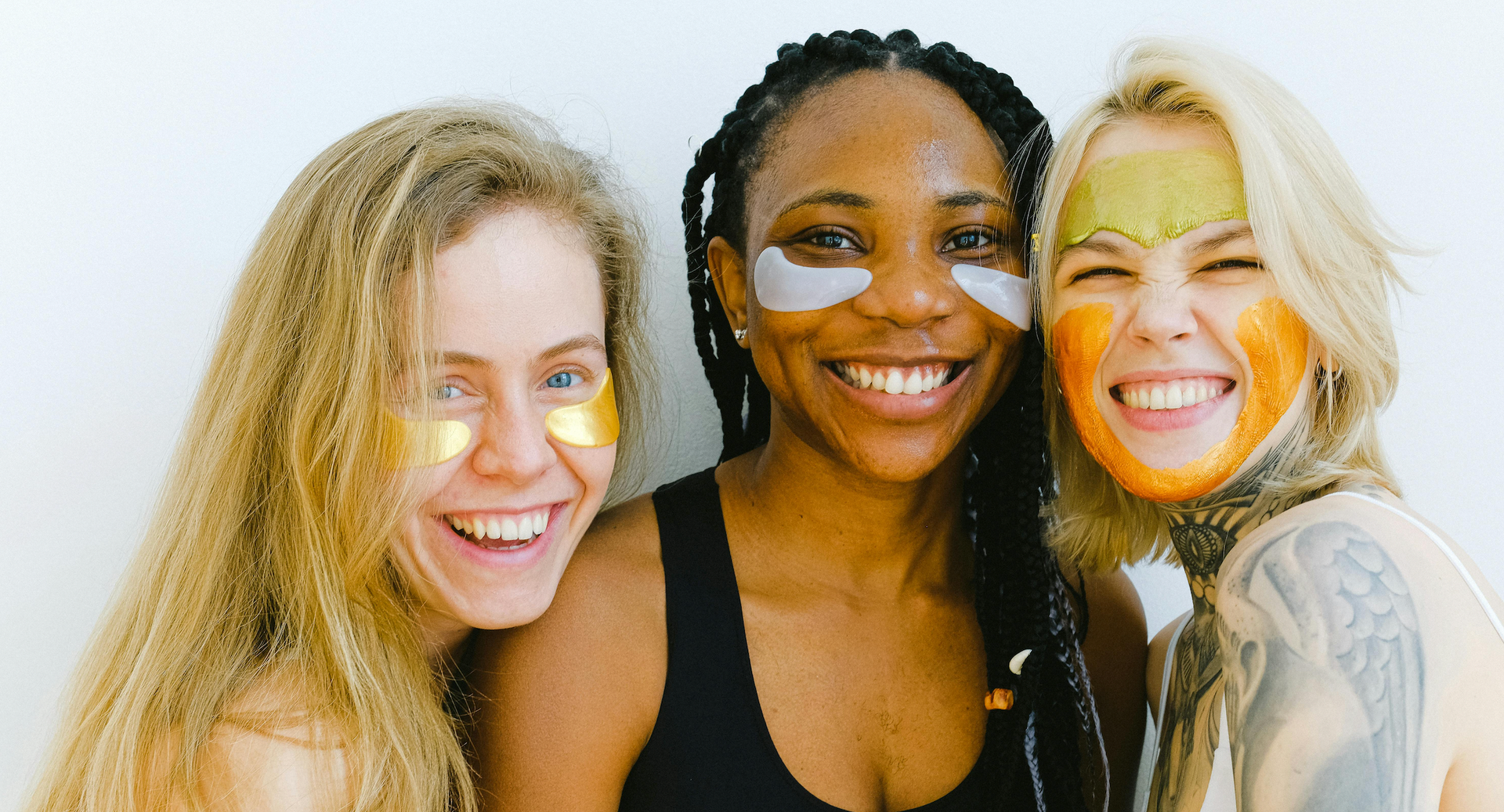 Three women with skincare masks smiling, close-up against a white background.