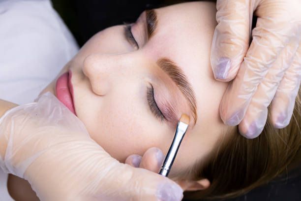 Woman receiving an eyebrow shaping treatment while laying down. Hands with gloves holding a pen and pointing.