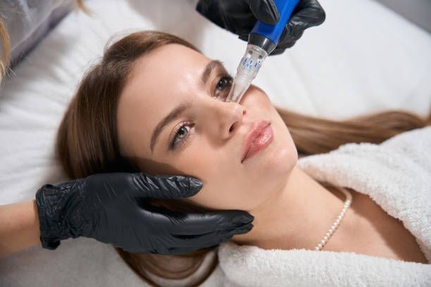 Woman receiving facial treatment; esthetician using device on her forehead. Indoors, white and pink colors.