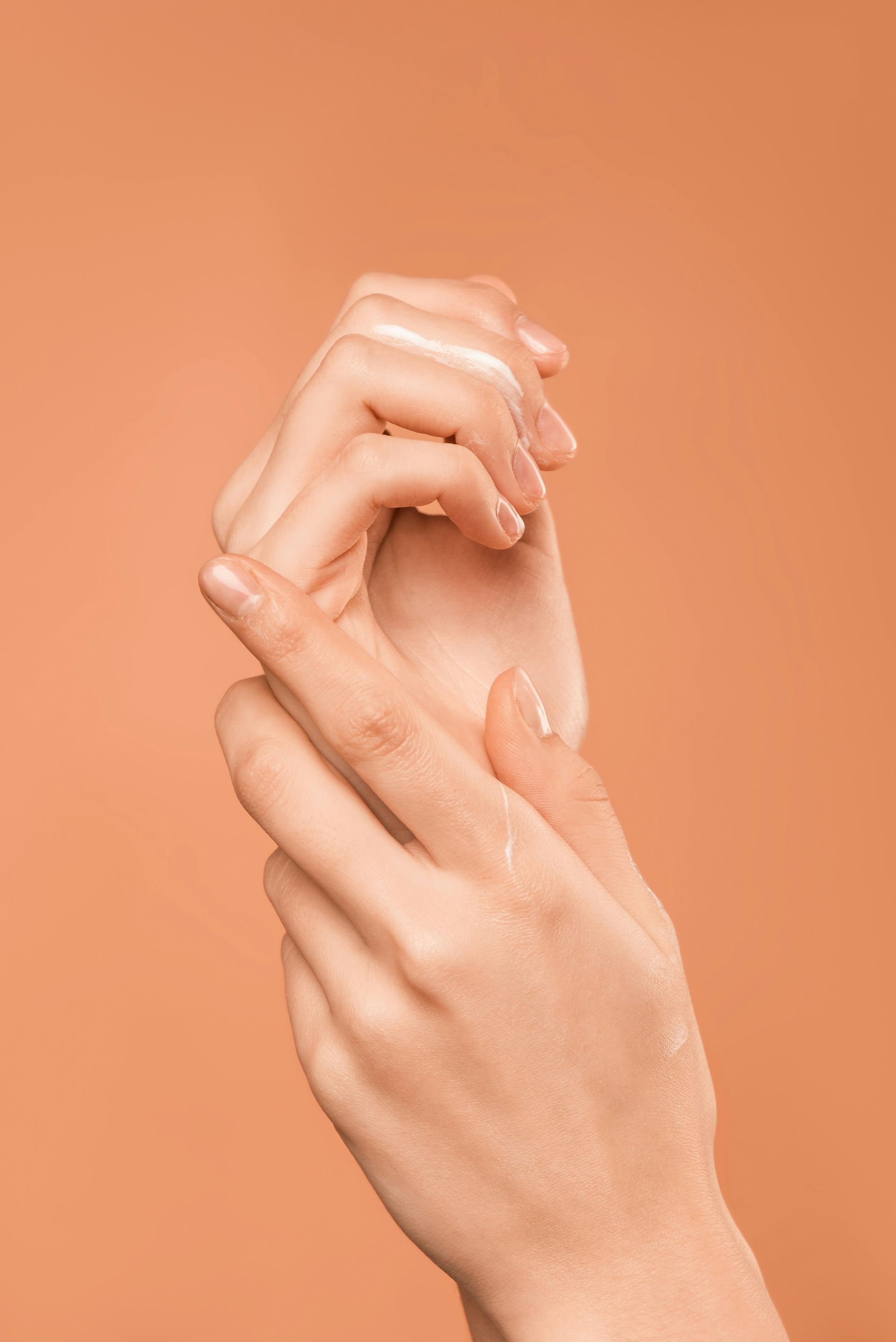 Hands, one clasping the other, against a peach background.