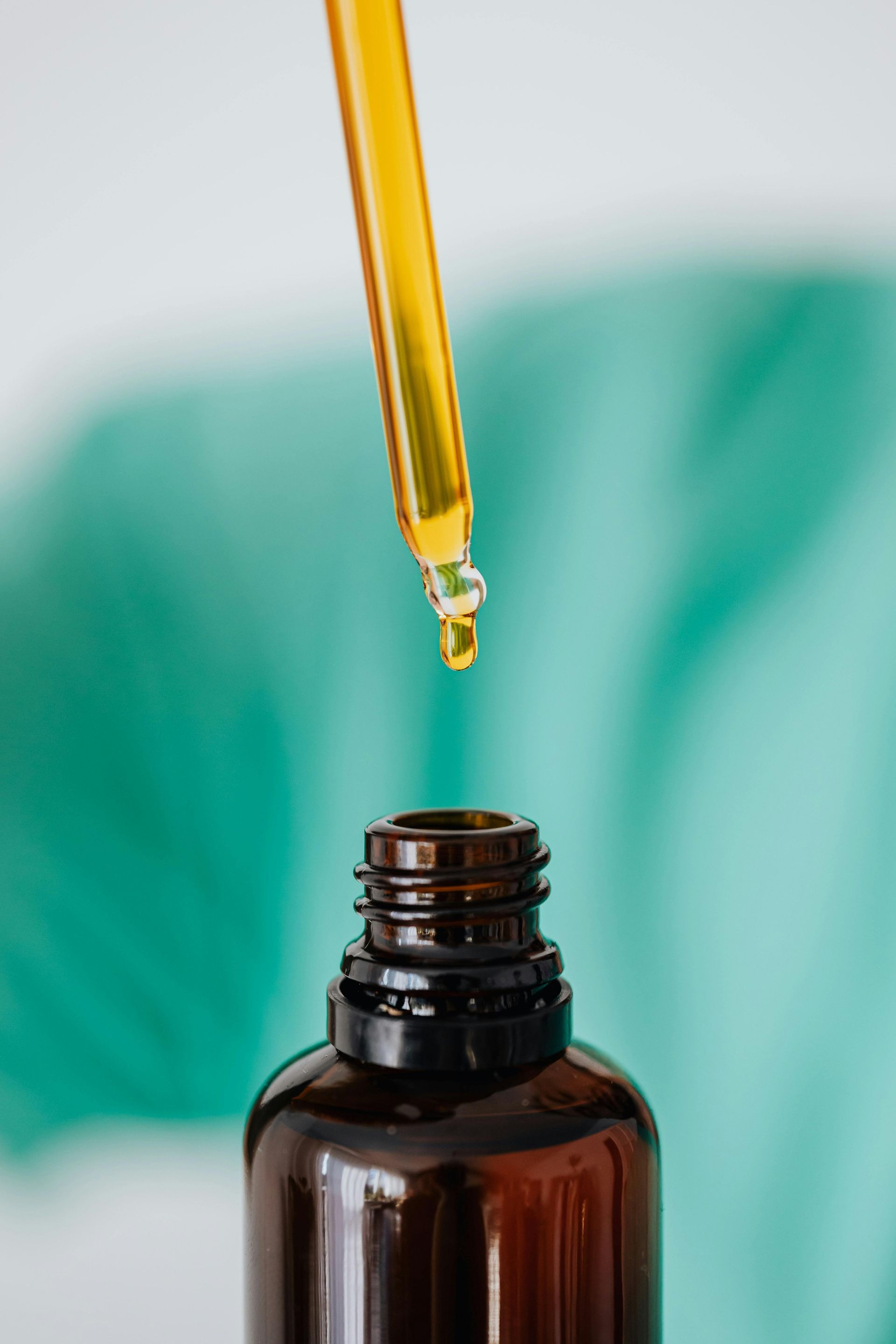 Amber liquid dripping from a dropper into a brown bottle, with a teal background.