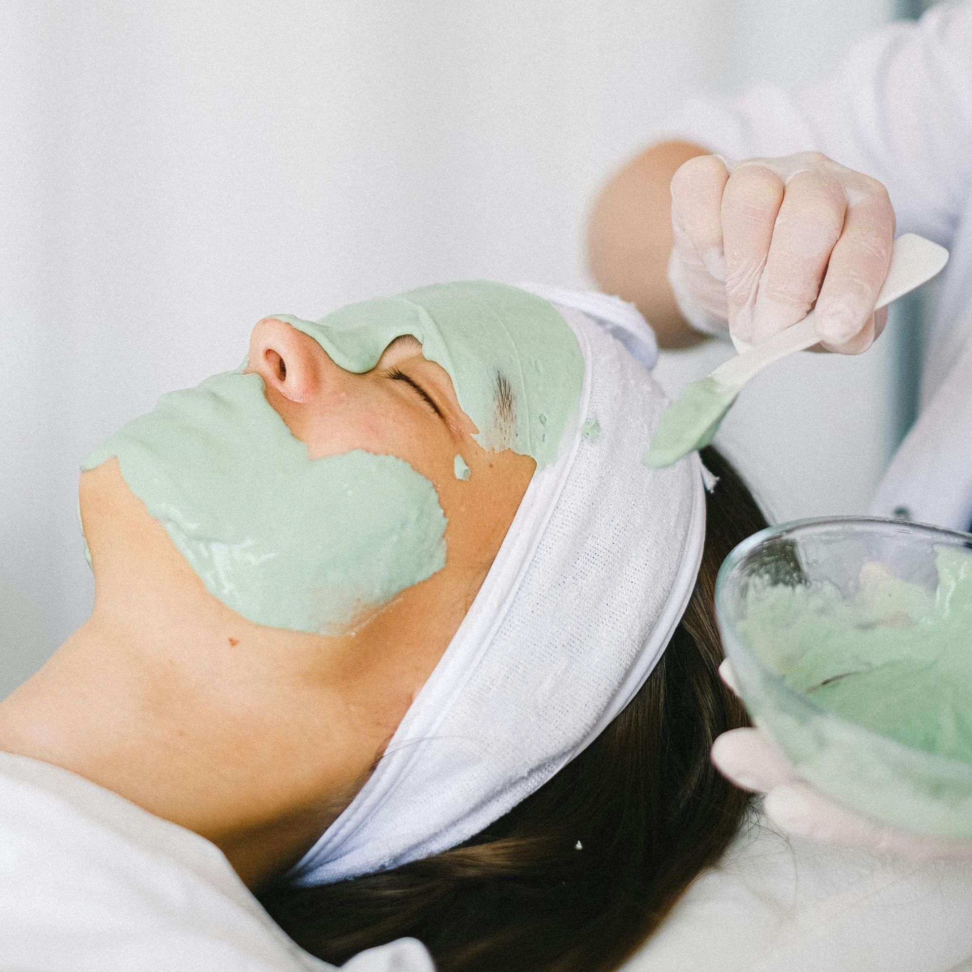 Person receiving a facial, with a green mask being applied in a spa setting.