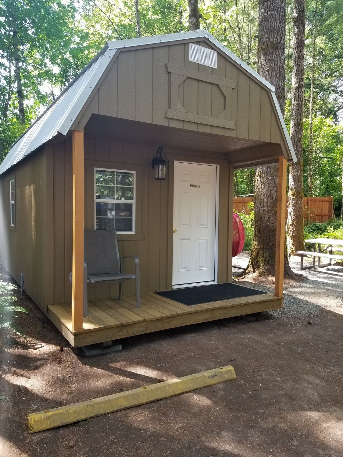 Small brown cabin with white door and porch in a wooded outdoor setting