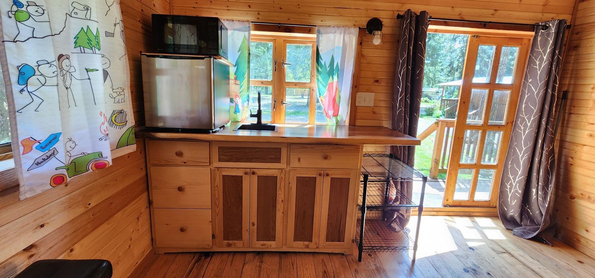Wooden cabin kitchen with cabinets, window, glass door, and sunlight streaming in