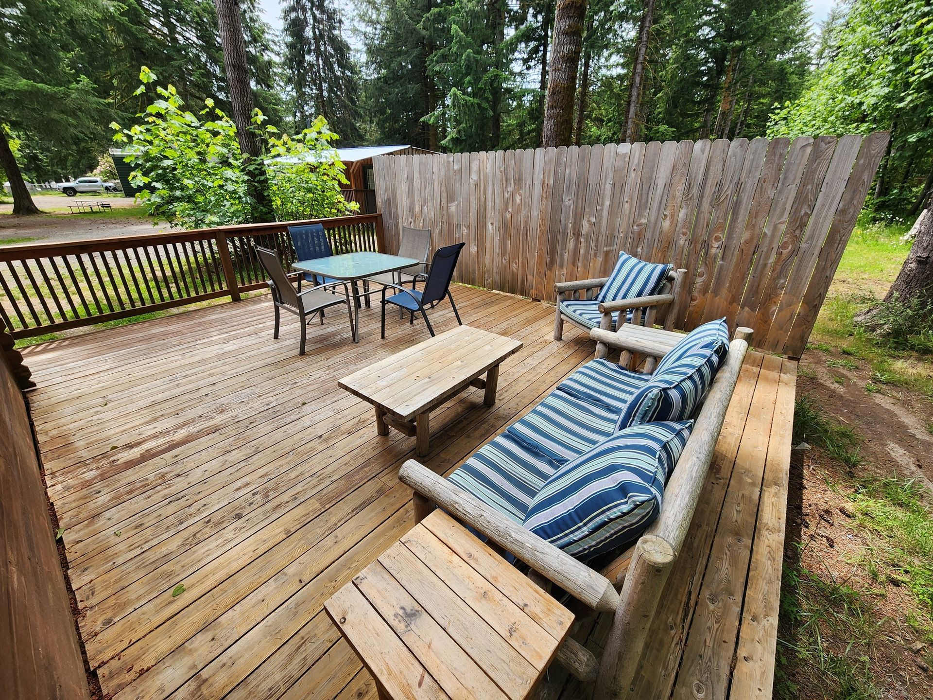 Wooden deck with outdoor seating, blue-striped cushions, and a fenced backyard surrounded by trees