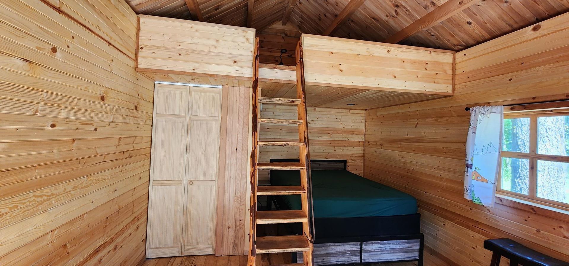 Rustic wooden loft room with ladder, bed, closet, and window.