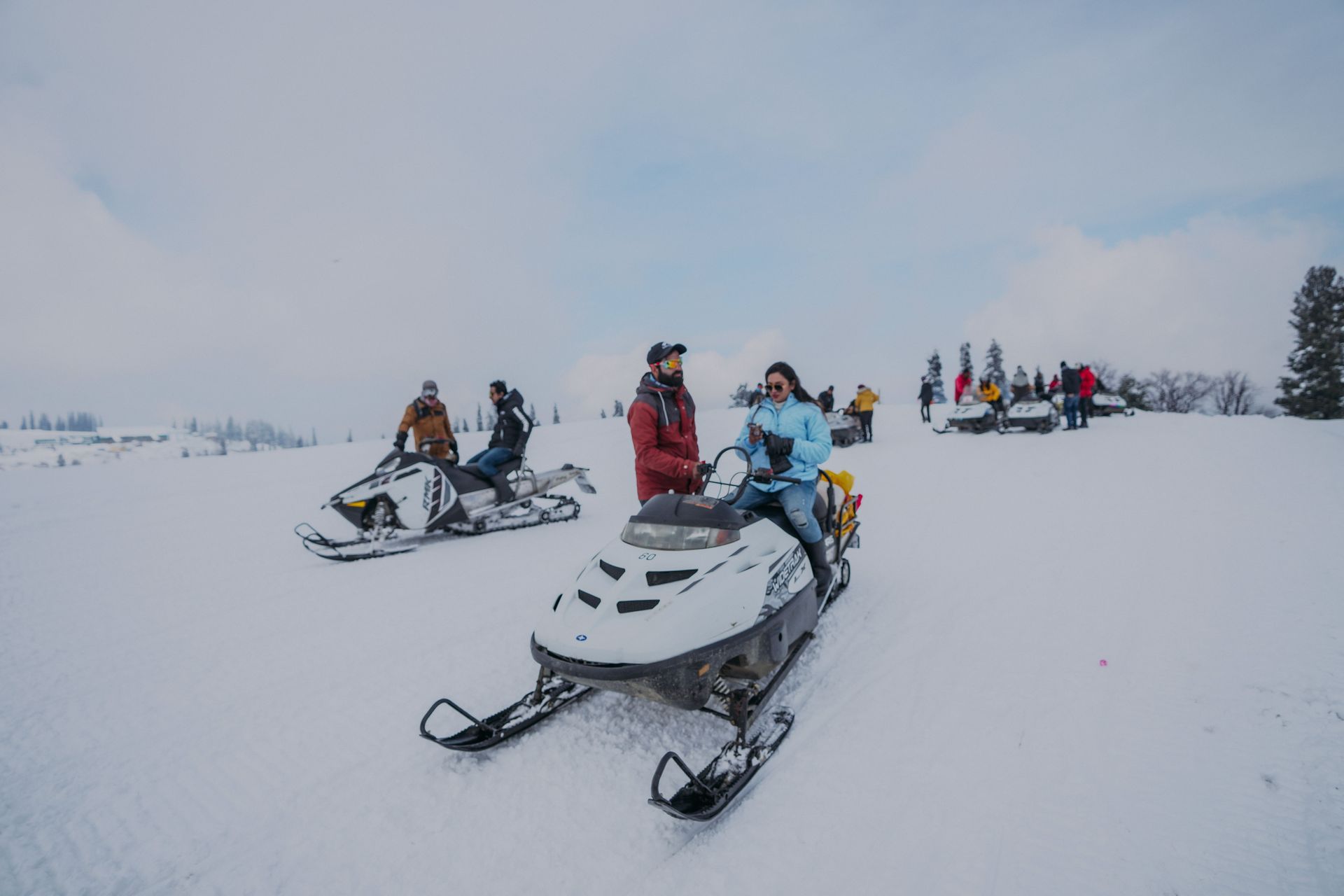 People riding snowmobiles on a snowy open plain under a cloudy sky