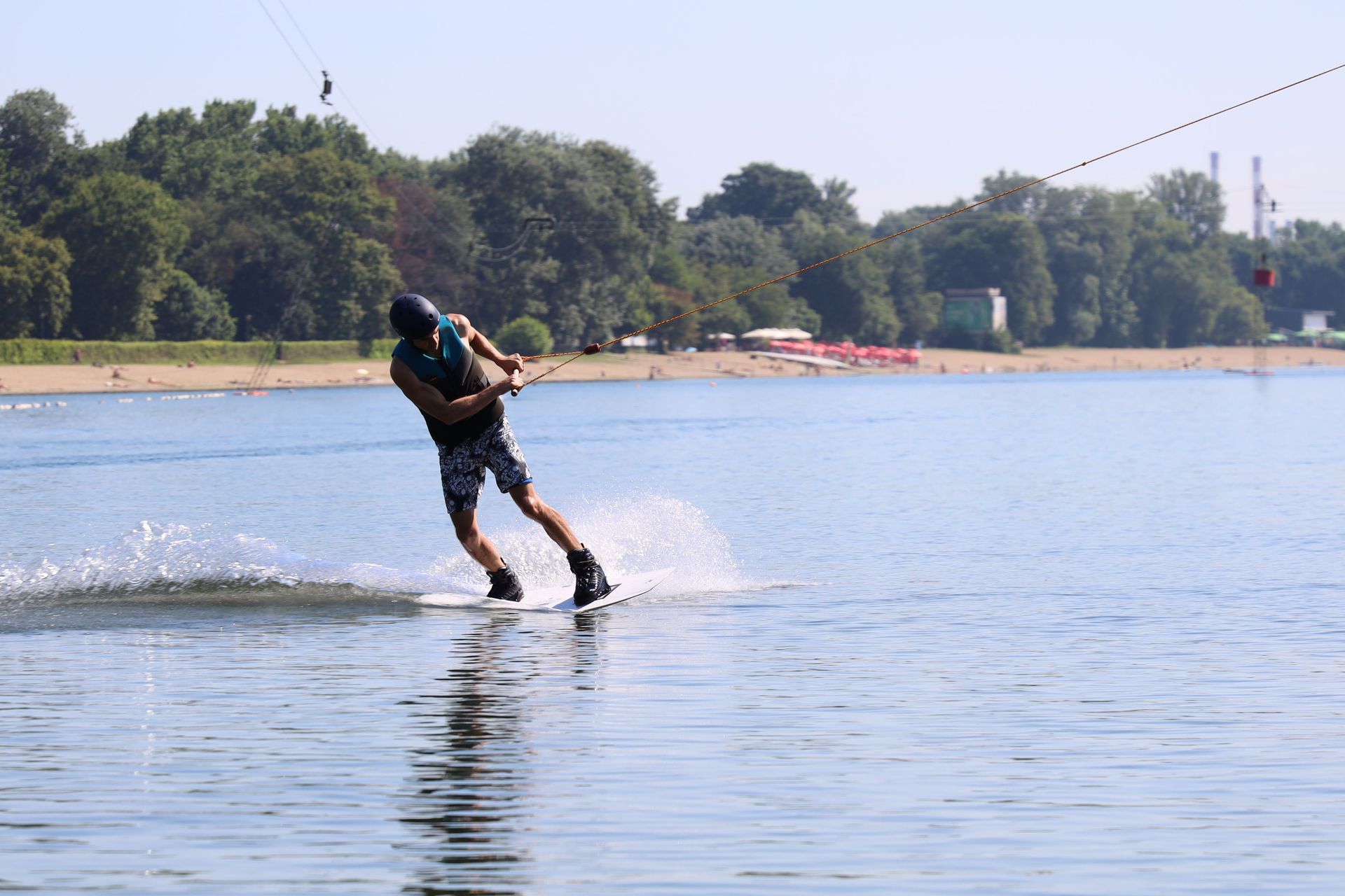 A person water skiing across a calm lake, leaning back and kicking up spray near a tree-lined shore.