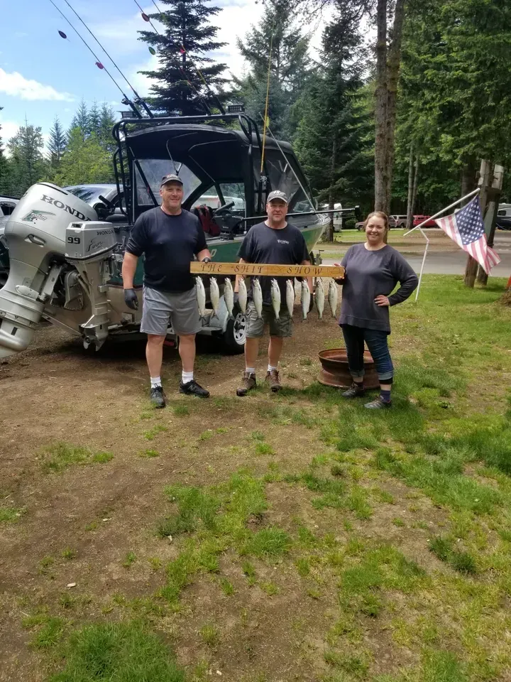 Three people posing beside a giant bullet sculpture in a grassy yard with trees and a truck.