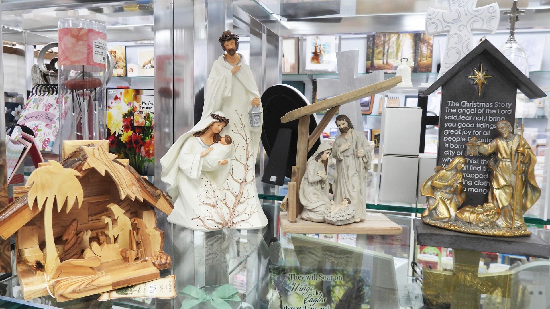 Nativity scene figurines in a store display: Mary, Joseph, baby Jesus, wooden stable, and crosses.