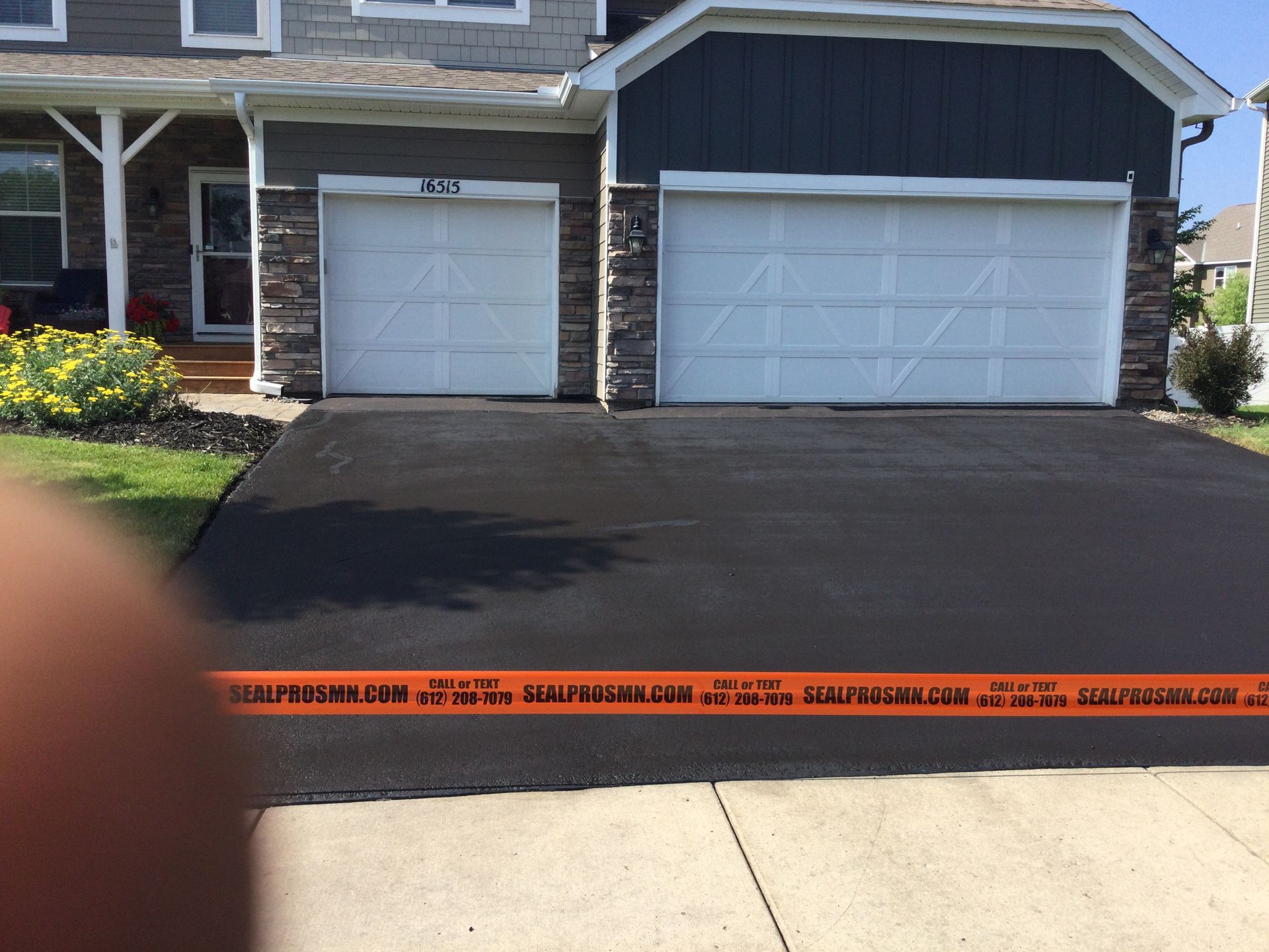 Newly paved black asphalt driveway in front of a two-car garage with caution tape across the foreground.