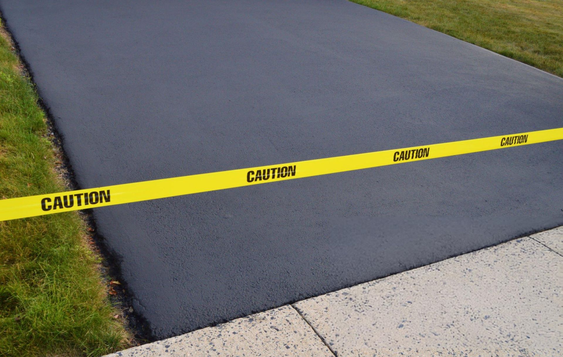 A newly seal-coated asphalt driveway against a sidewalk