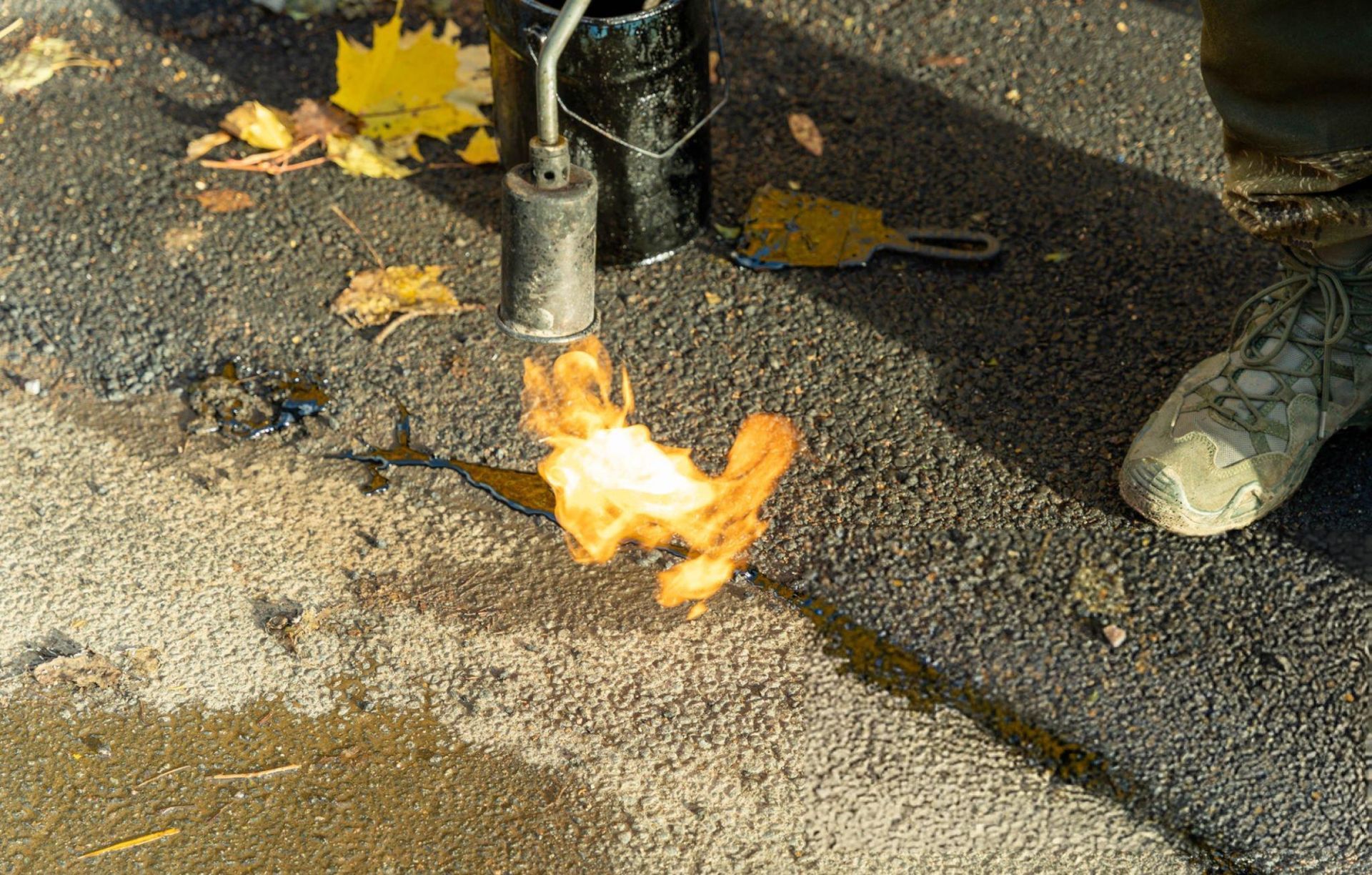 Worker using a gas burner to meticulously apply mastic sealant to cracks in an asphalt surface