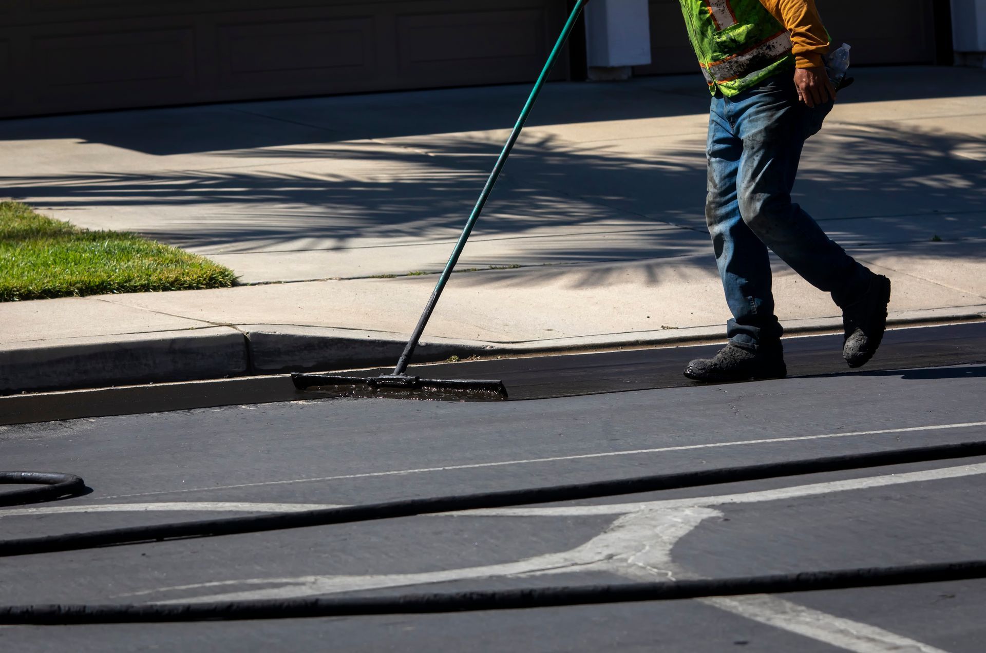 Worker applying fresh asphalt with a long-handled squeegee on a roadway.
