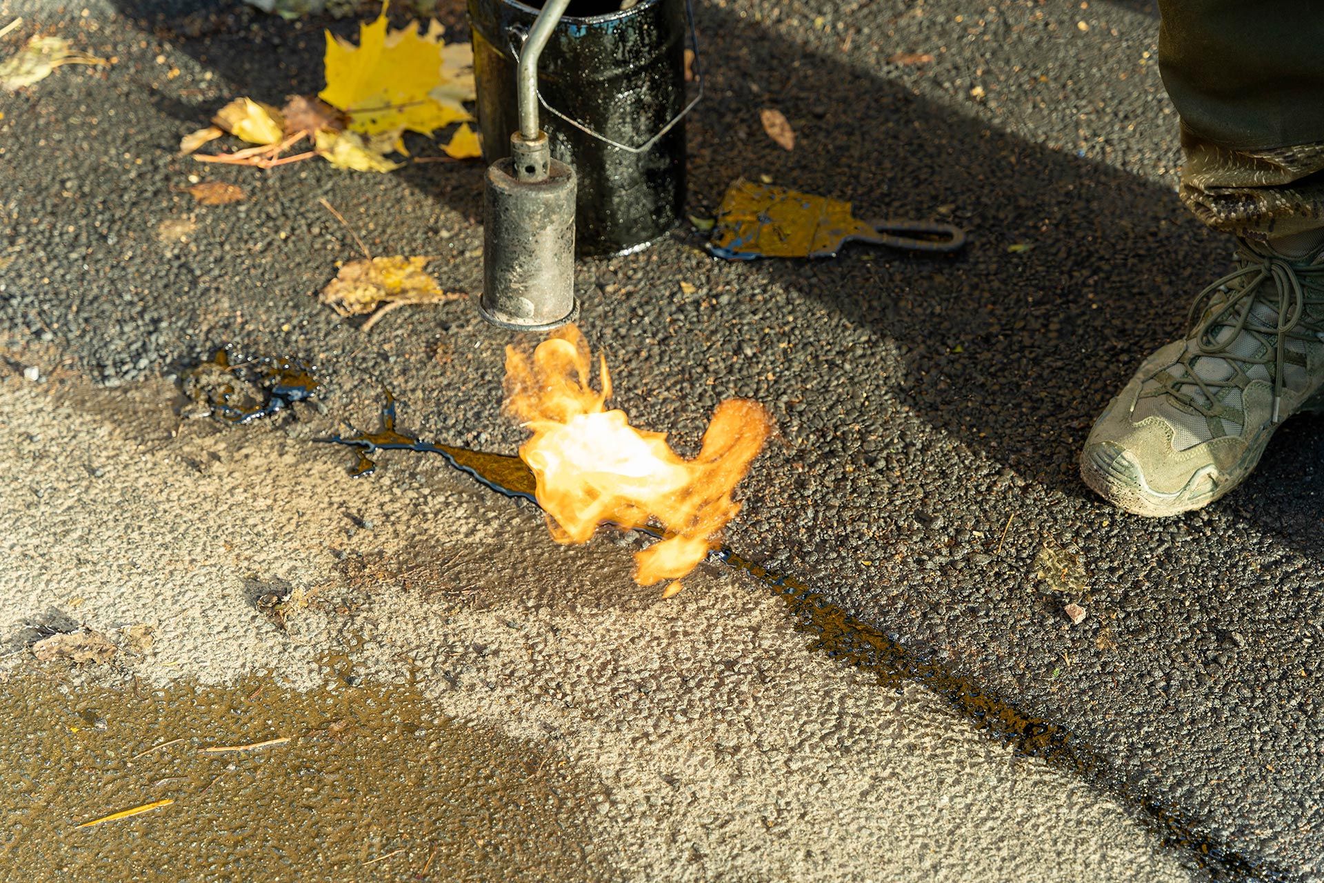 Flame heating and sealing a crack in asphalt pavement during road repair work.