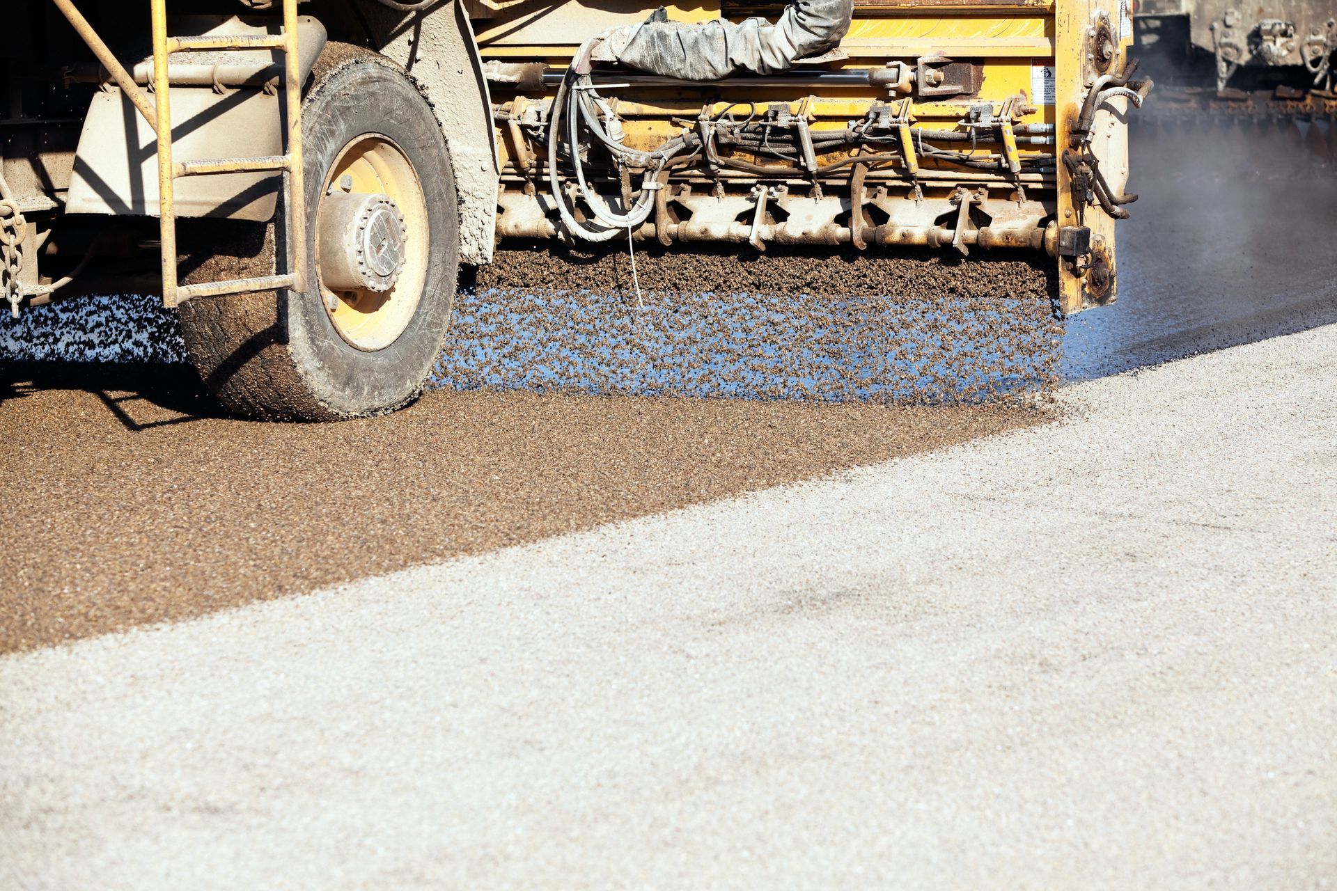 Road construction vehicle spreading asphalt on a surface.
