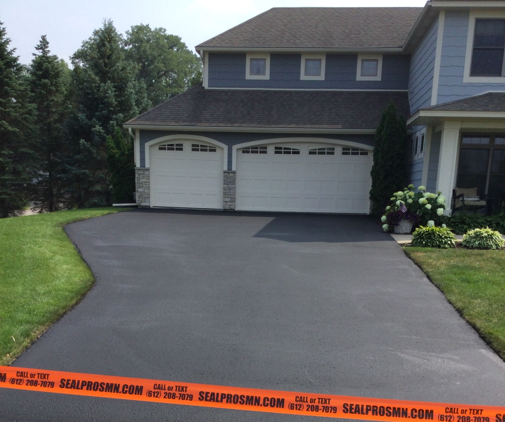 Driveway leading to a two-story blue house with a two-car garage and lush green lawn.