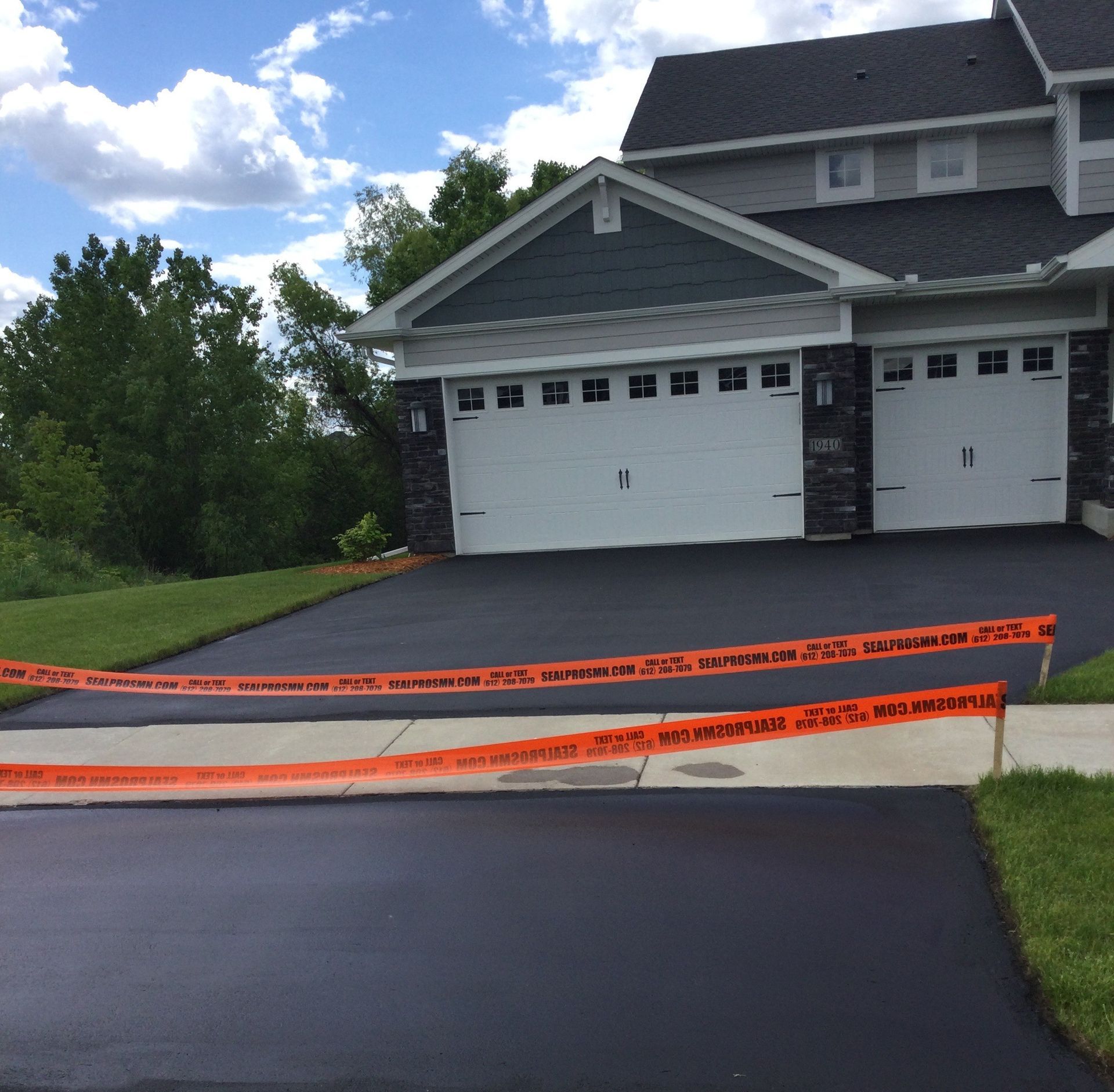 Newly paved asphalt driveway with orange caution tape in front of a two-car garage.