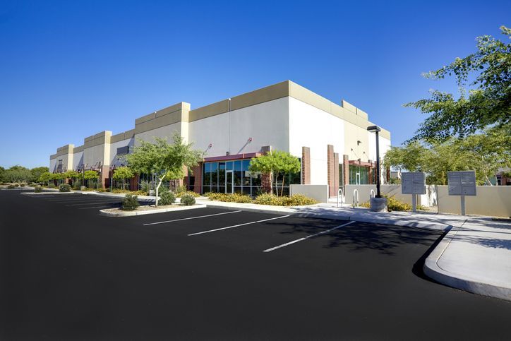 A modern building with large windows, trees, and an empty lot under a clear sky