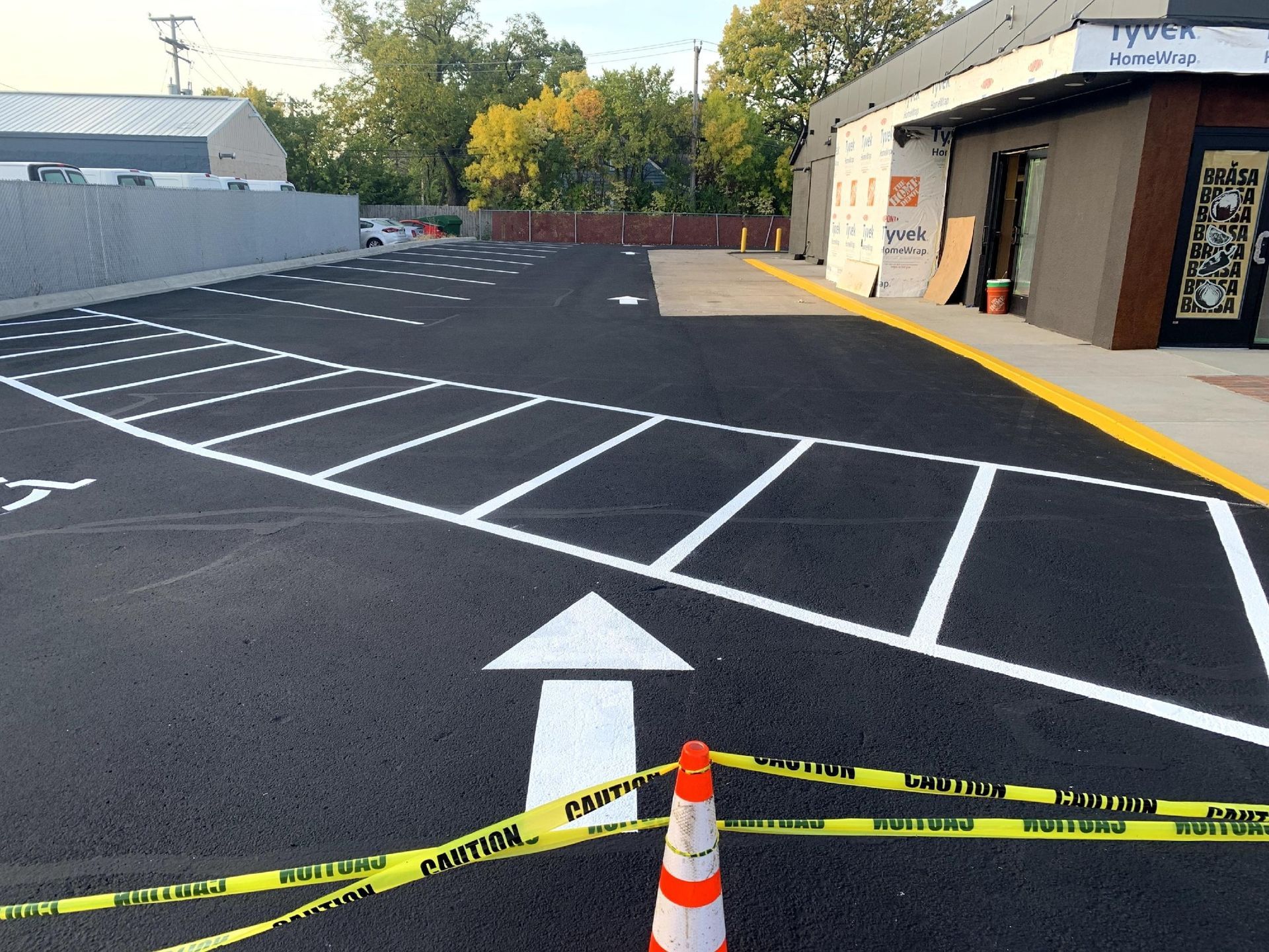 Newly paved parking lot with white parking space lines and directional arrow. Yellow caution tape in foreground.
