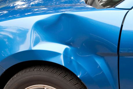 A close up of a blue car with a damaged fender.