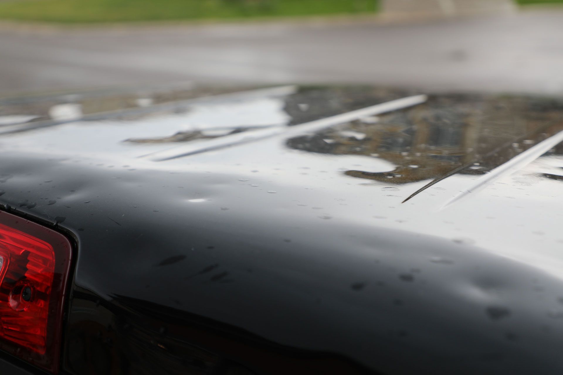A close up of a black car 's hood and tail light.
