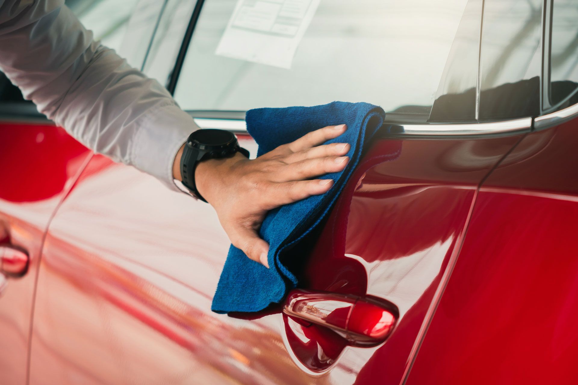 A person is cleaning a red car with a blue towel.