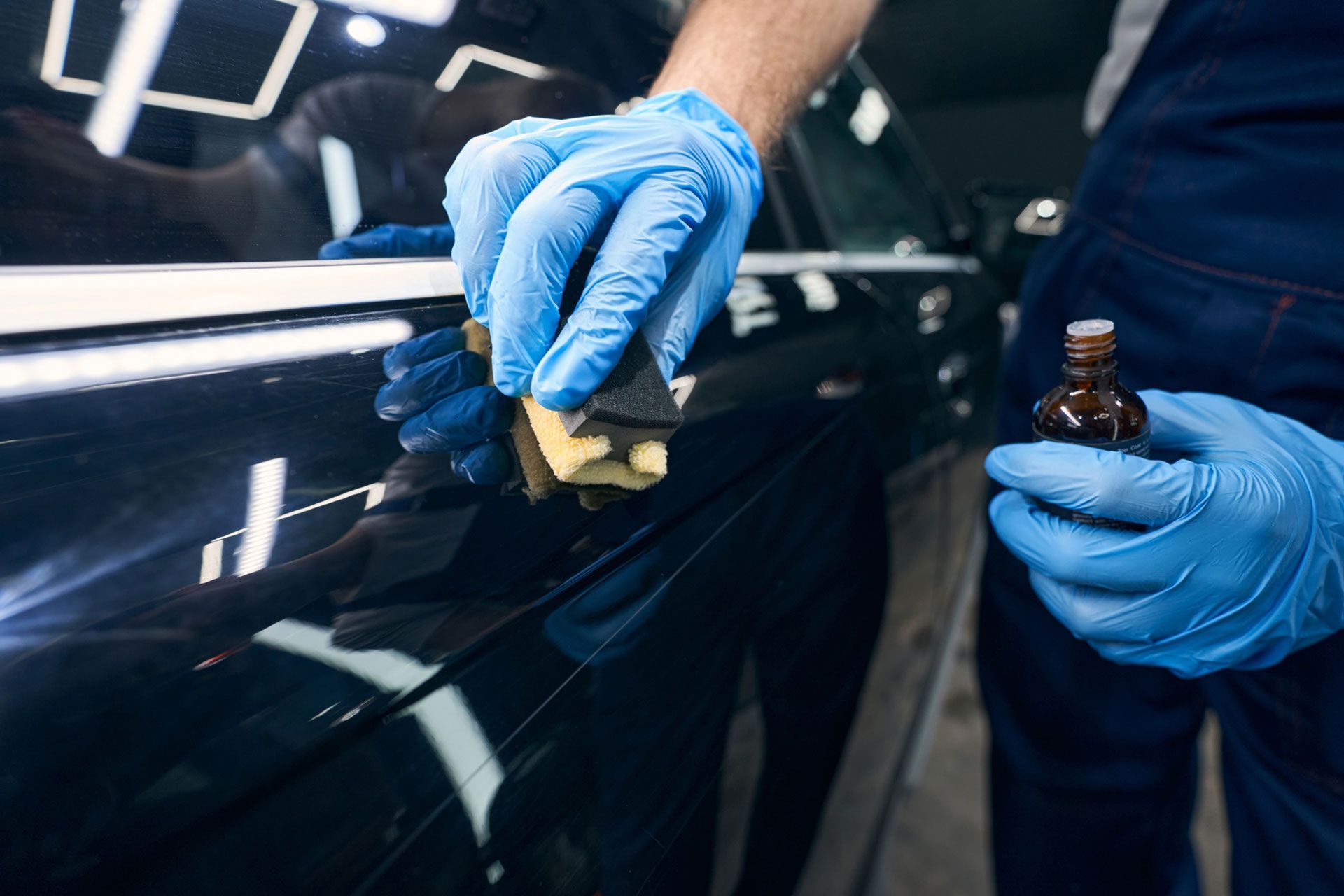 A man wearing blue gloves is polishing a car with a sponge.