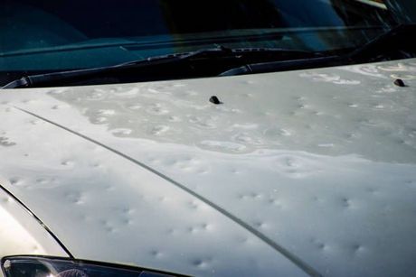 A white car with hail damage to the hood and windshield.