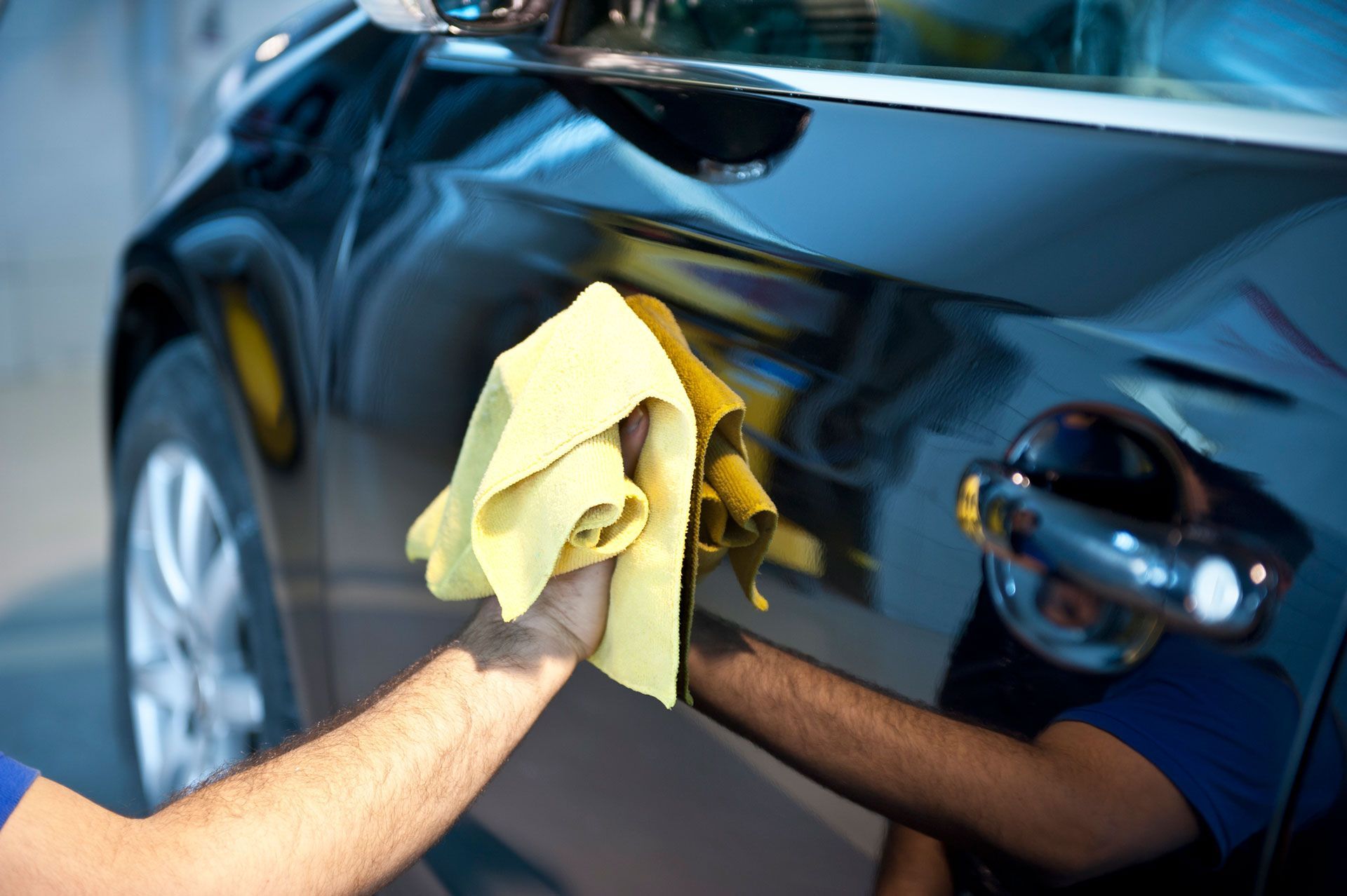 A man is cleaning a car with a yellow cloth.