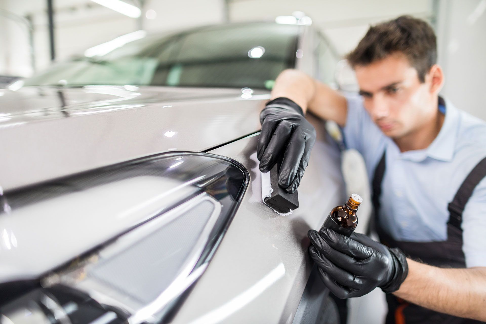 A man is polishing the front of a car in a garage.