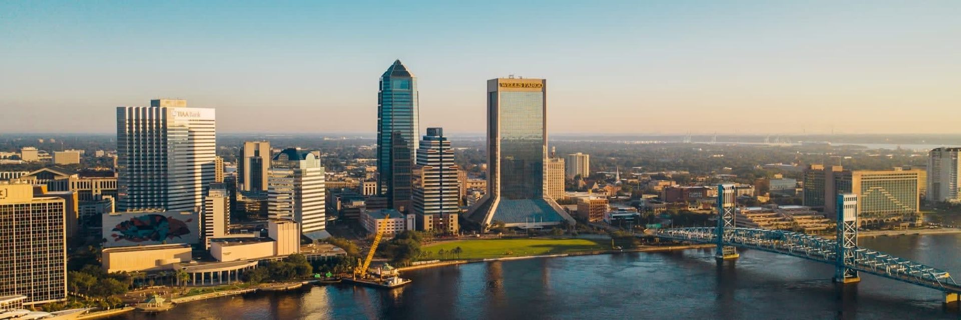 Aerial view of Jacksonville, Florida, skyline at sunset, with skyscrapers, a river, and bridge.