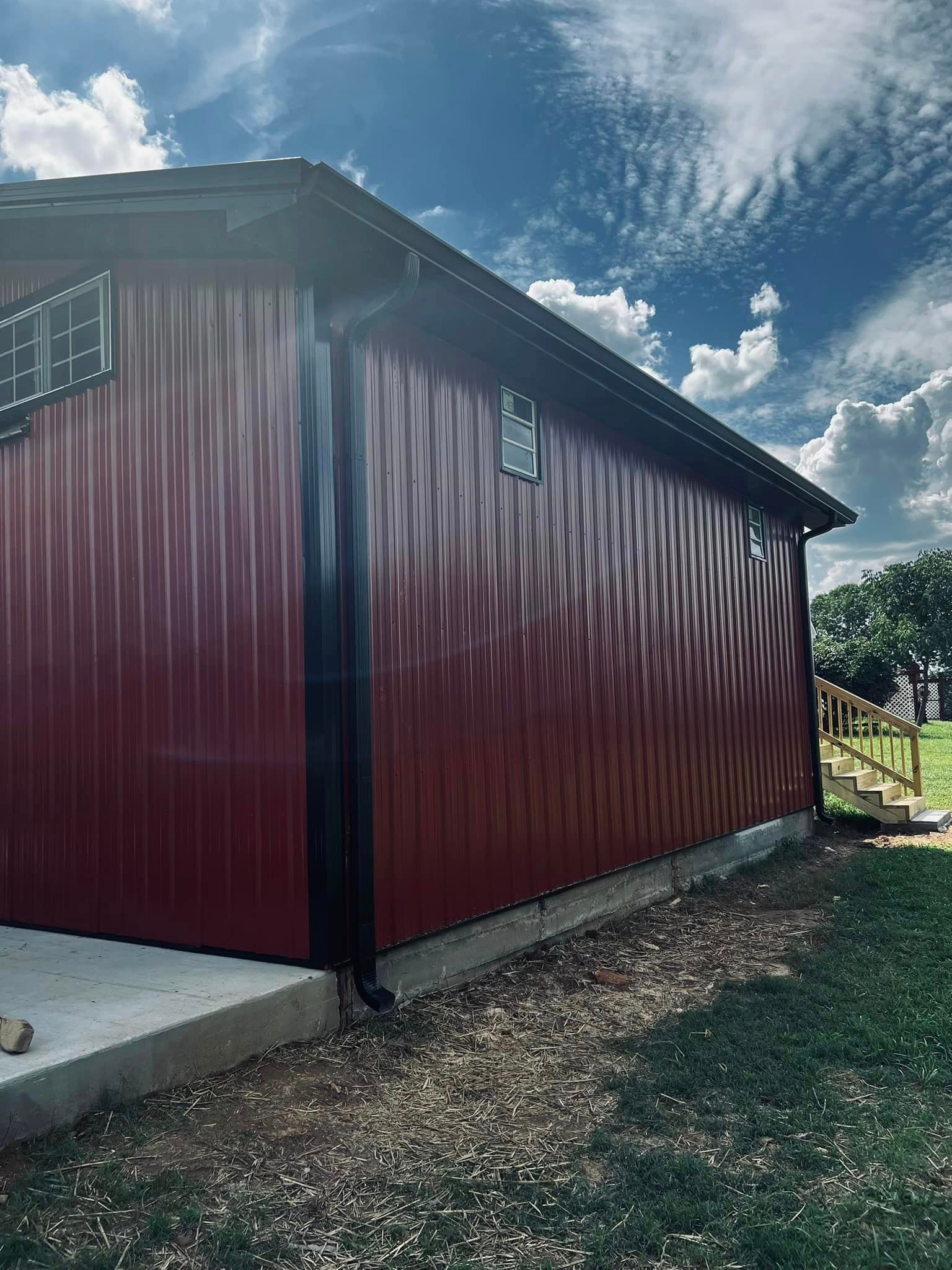 A red metal building with a black roof is sitting on top of a lush green field.