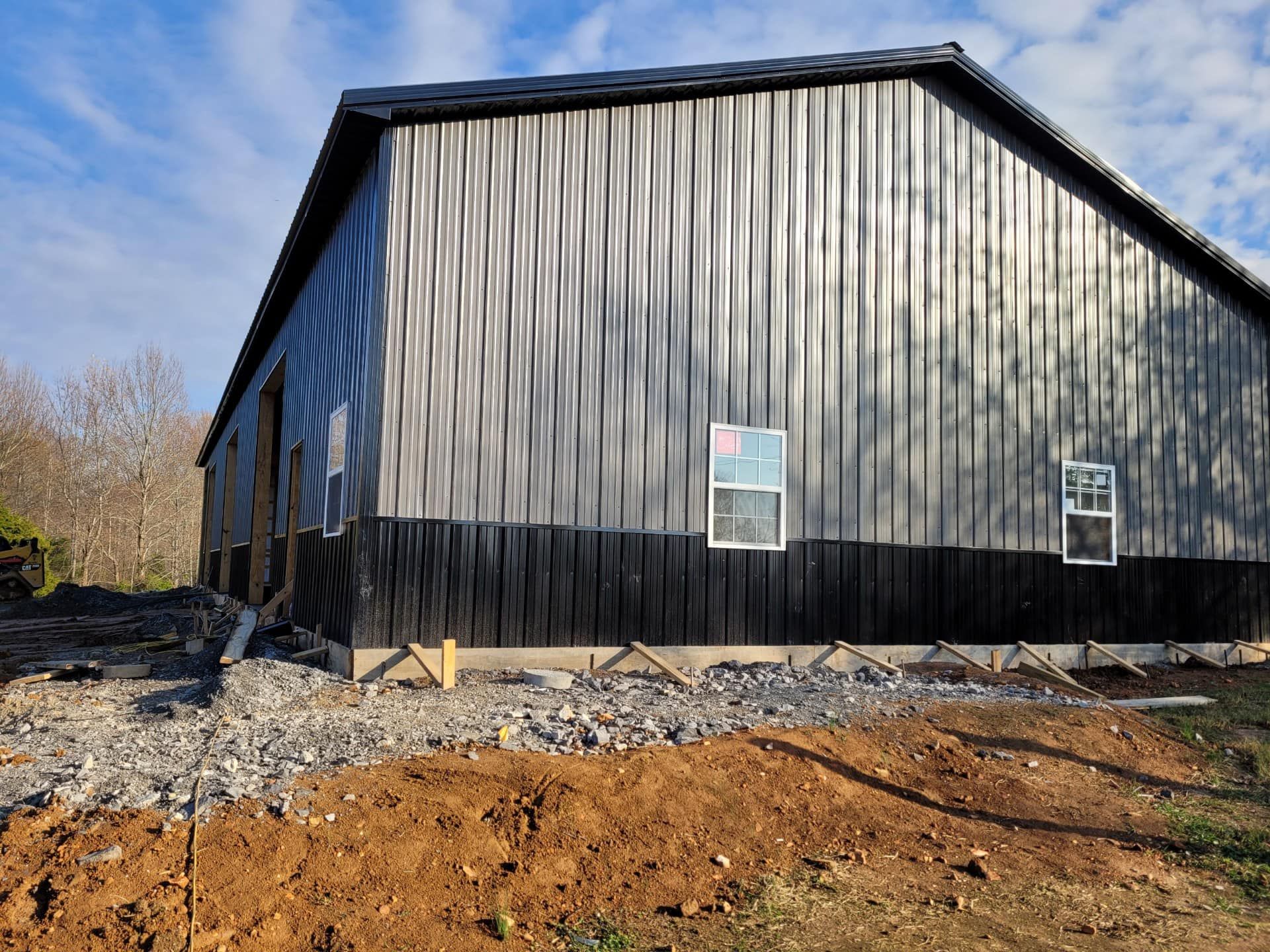A large metal barn is being built in the middle of a dirt field.