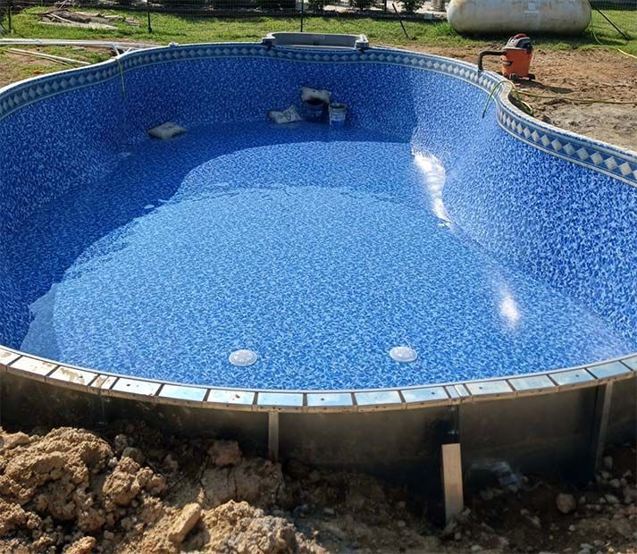 A large blue swimming pool is being built in the dirt.