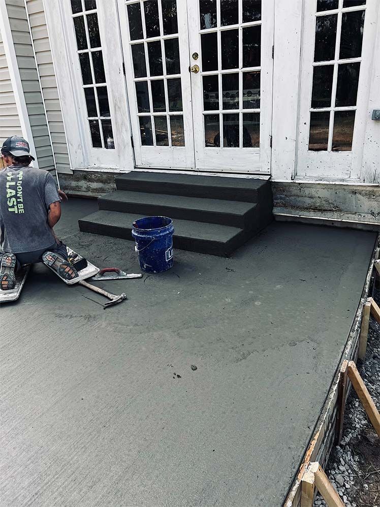 A man is kneeling down on a concrete patio in front of a house.