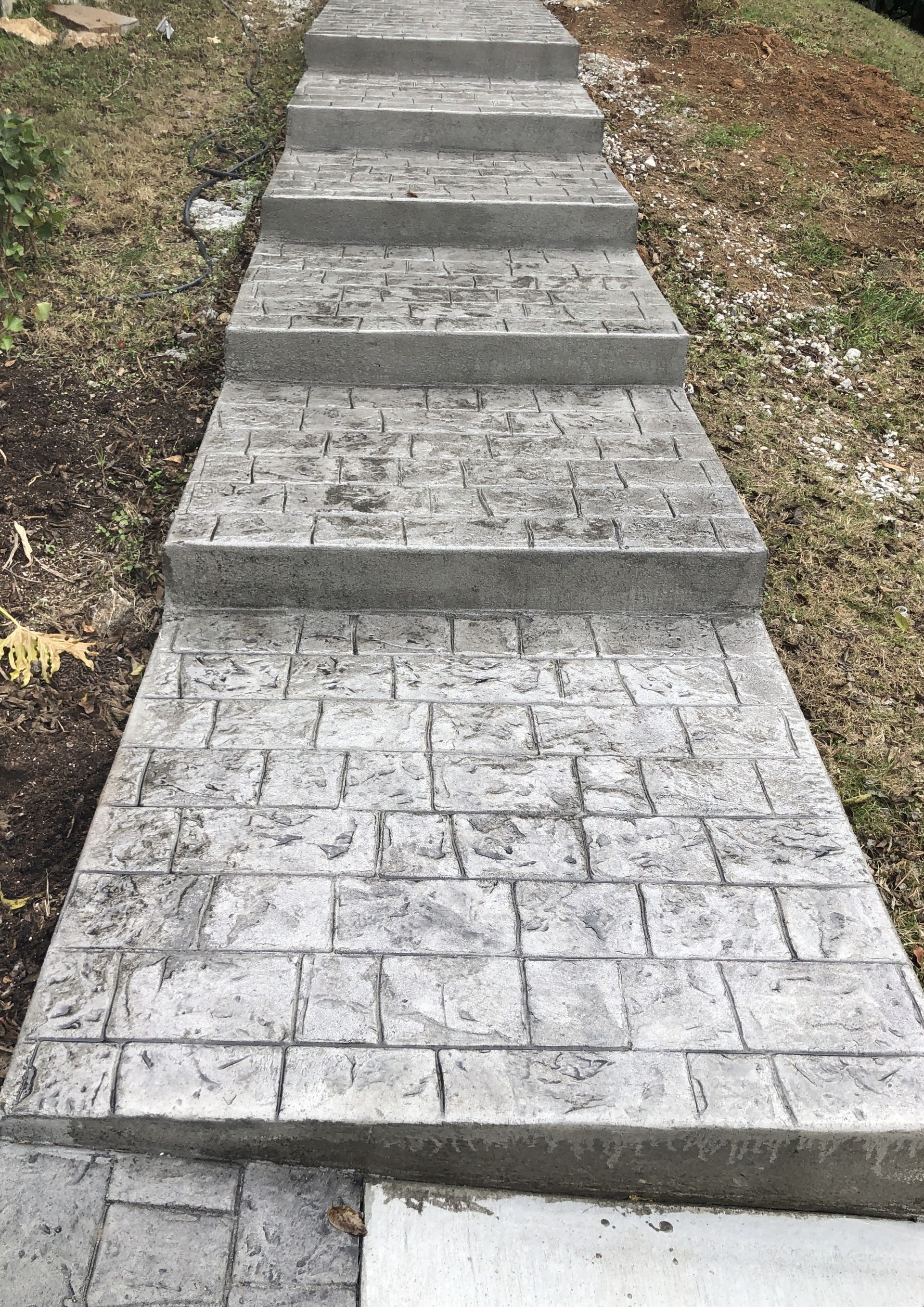 A concrete walkway with stairs leading up to a grassy area.