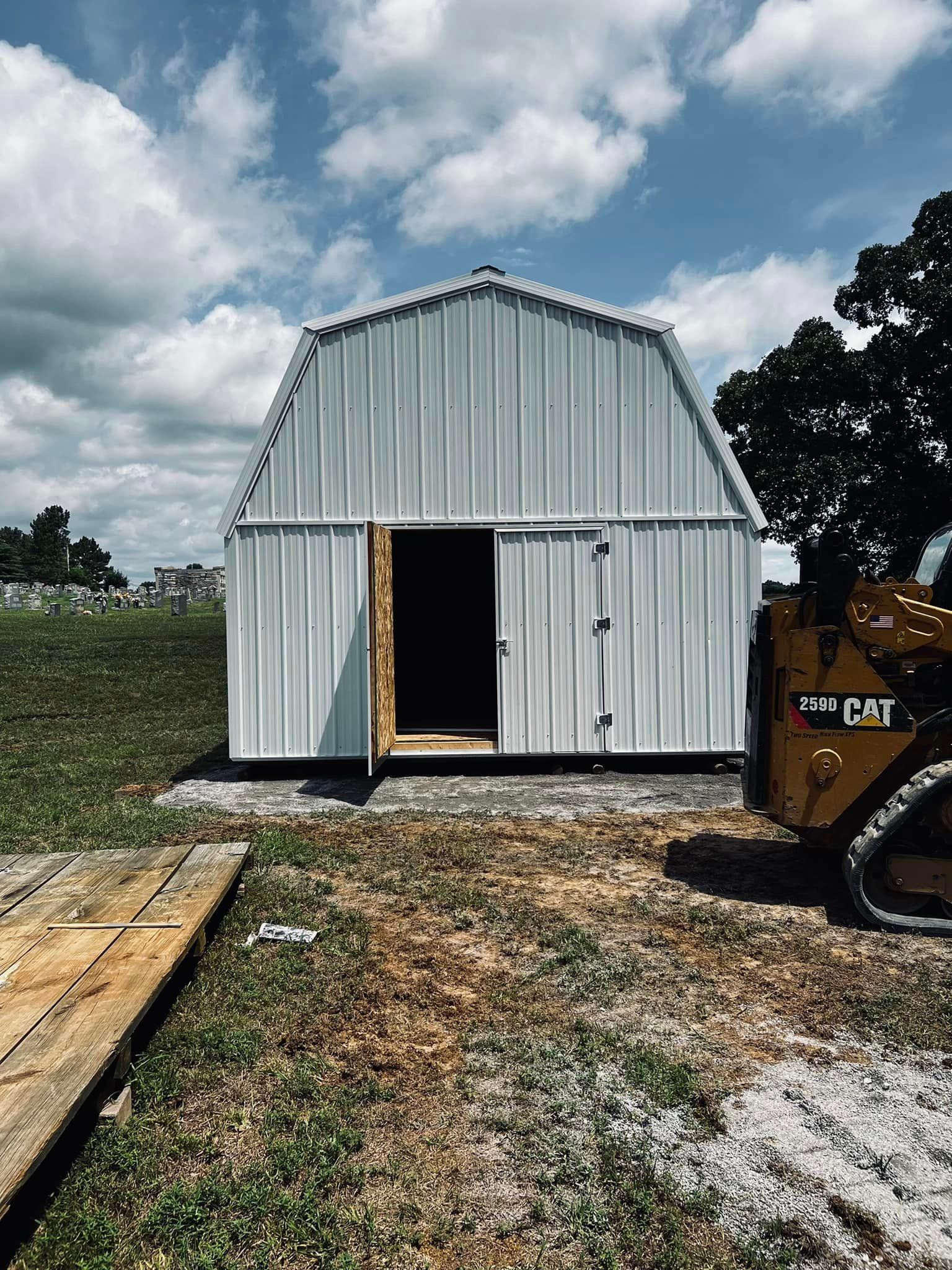 A white barn is being built in a field next to a bulldozer.