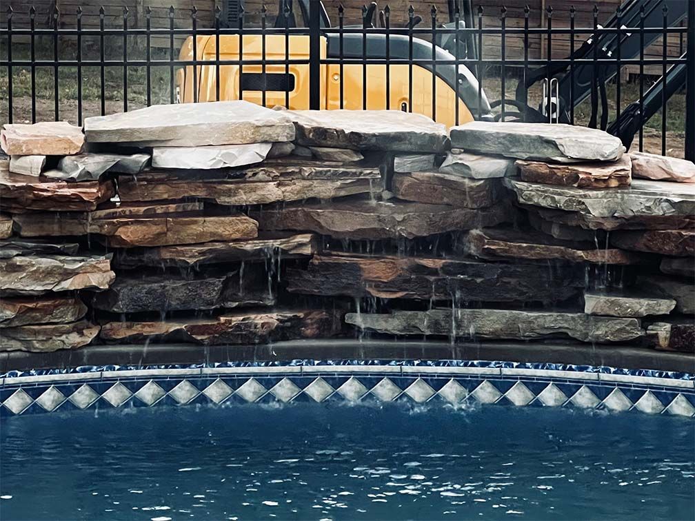 A pool with a waterfall and a fence in the background