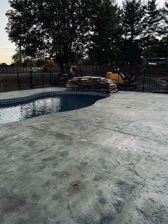 A large swimming pool is surrounded by a fence and trees.