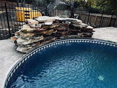 A large swimming pool surrounded by rocks and a fence.