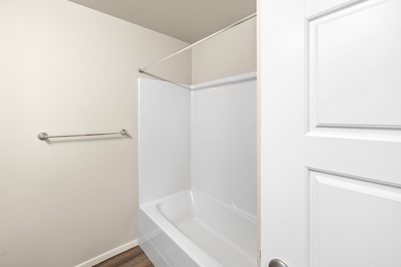 Bathroom with a tub/shower combo, white tile surround, towel bar, and a white door.