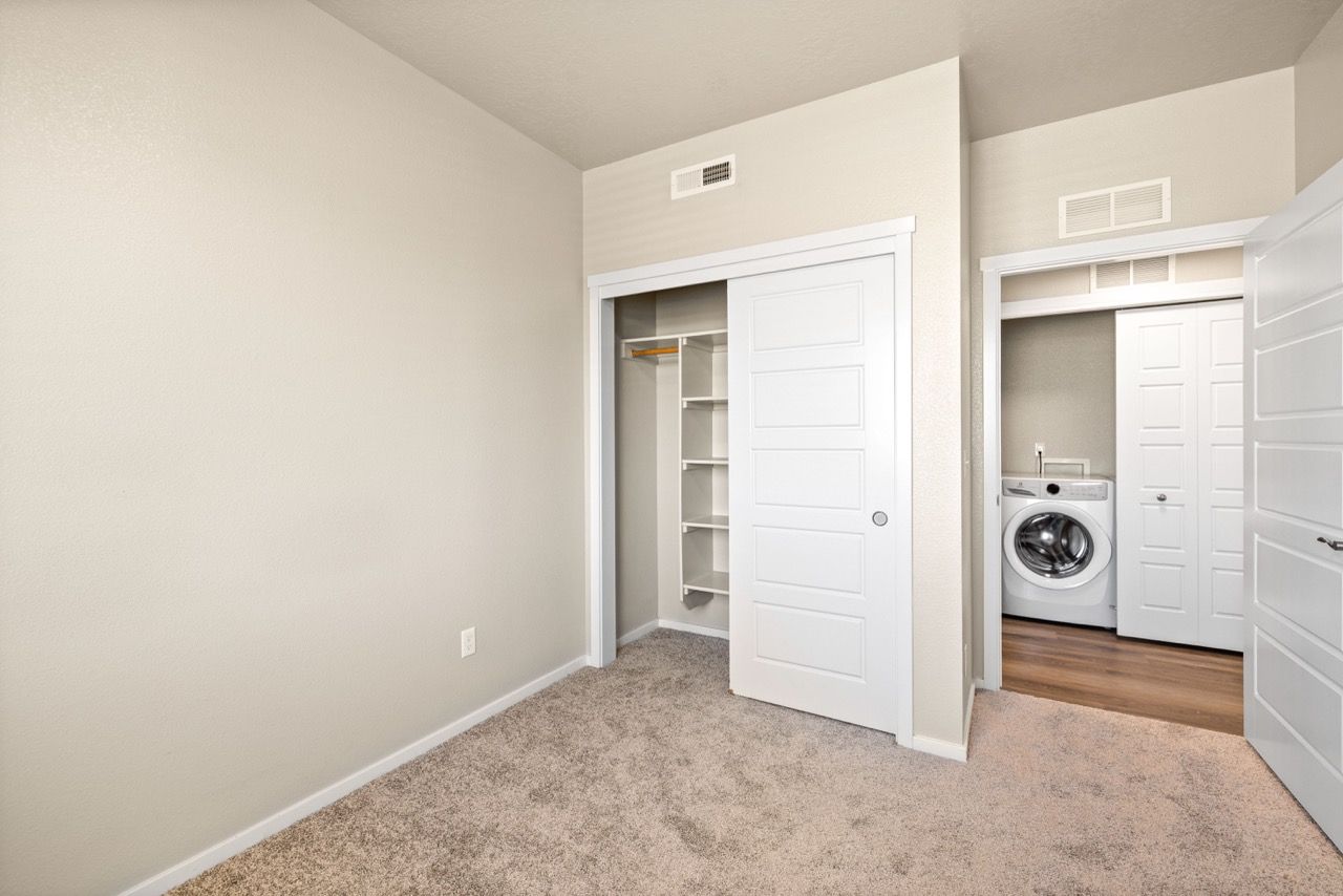 Bedroom with beige walls, carpet, a closet, and a doorway to a laundry area with a washer.