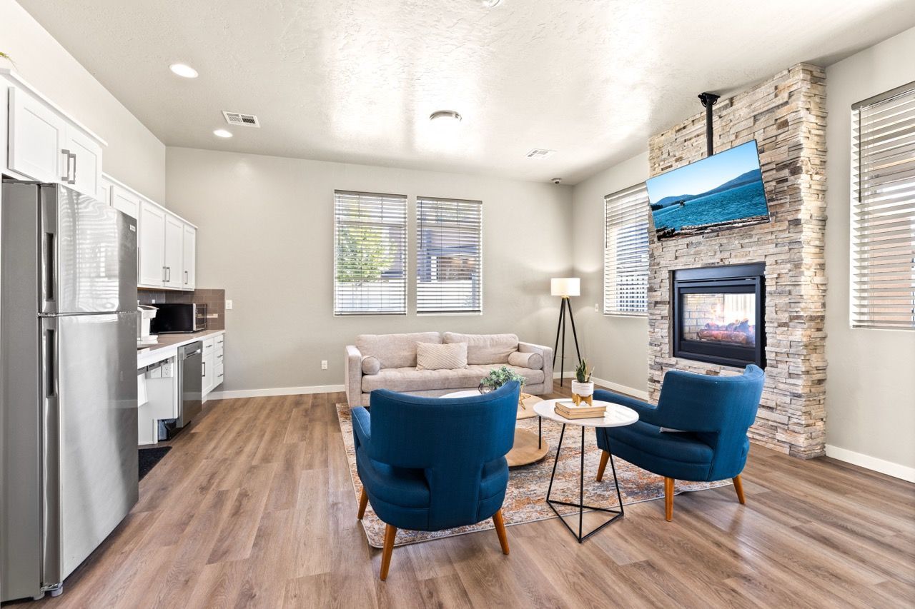 Open-concept living area with kitchen, sofa, blue chairs, stone fireplace, and mounted TV.