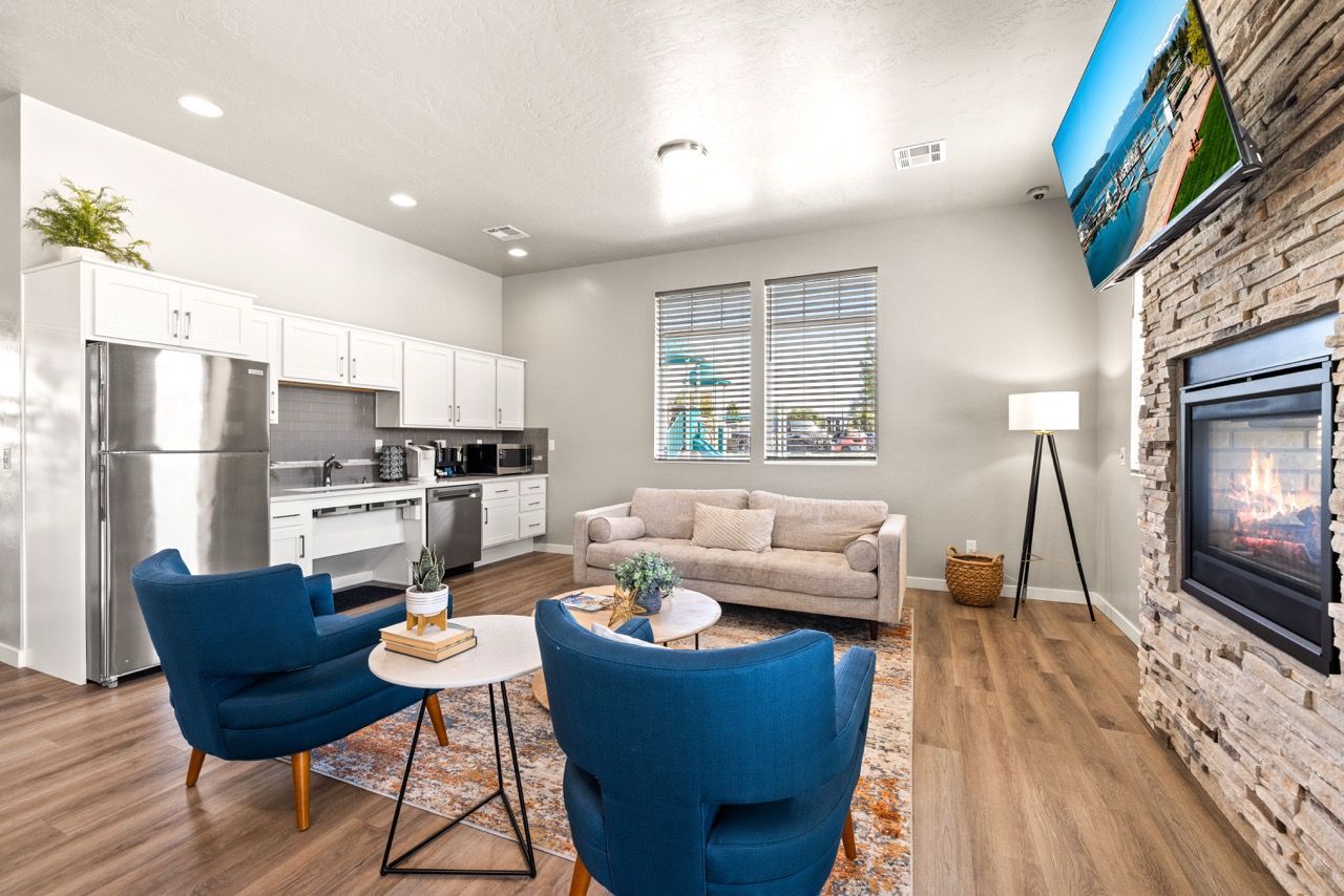 Bright living area with beige sofa, two blue chairs, a gas fireplace, mounted TV, and white kitchen cabinets.