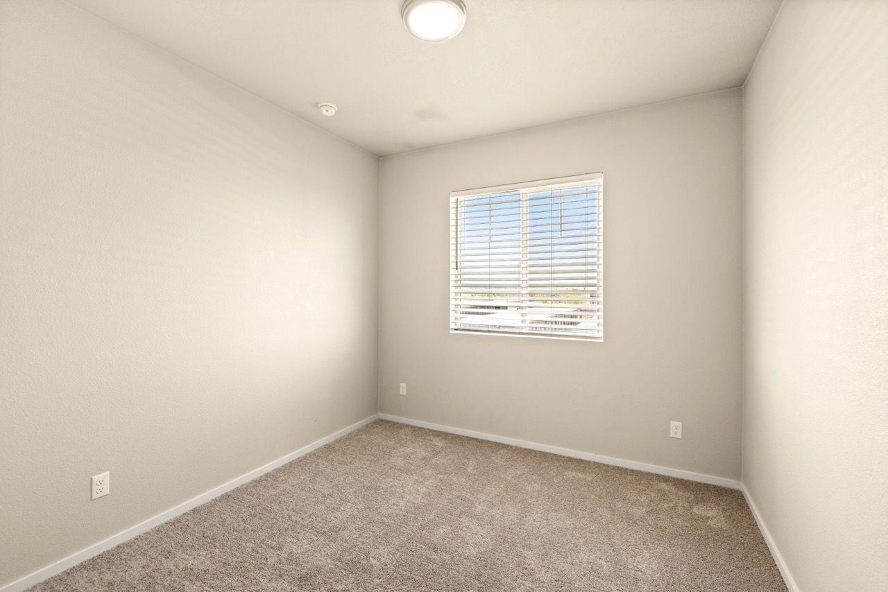 Empty bedroom with beige walls, carpet, and a window with blinds.