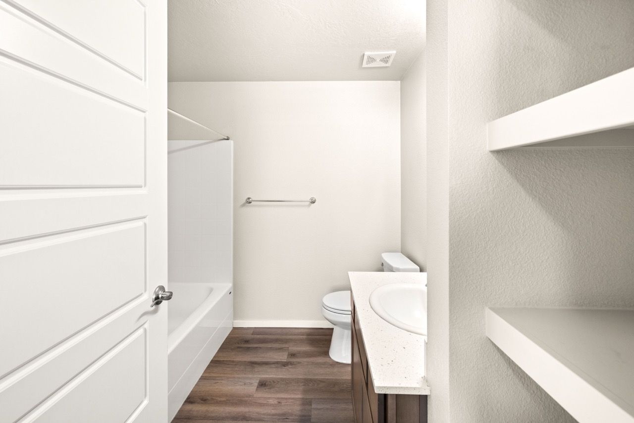 White bathroom with tub/shower, toilet, and vanity sink with storage.