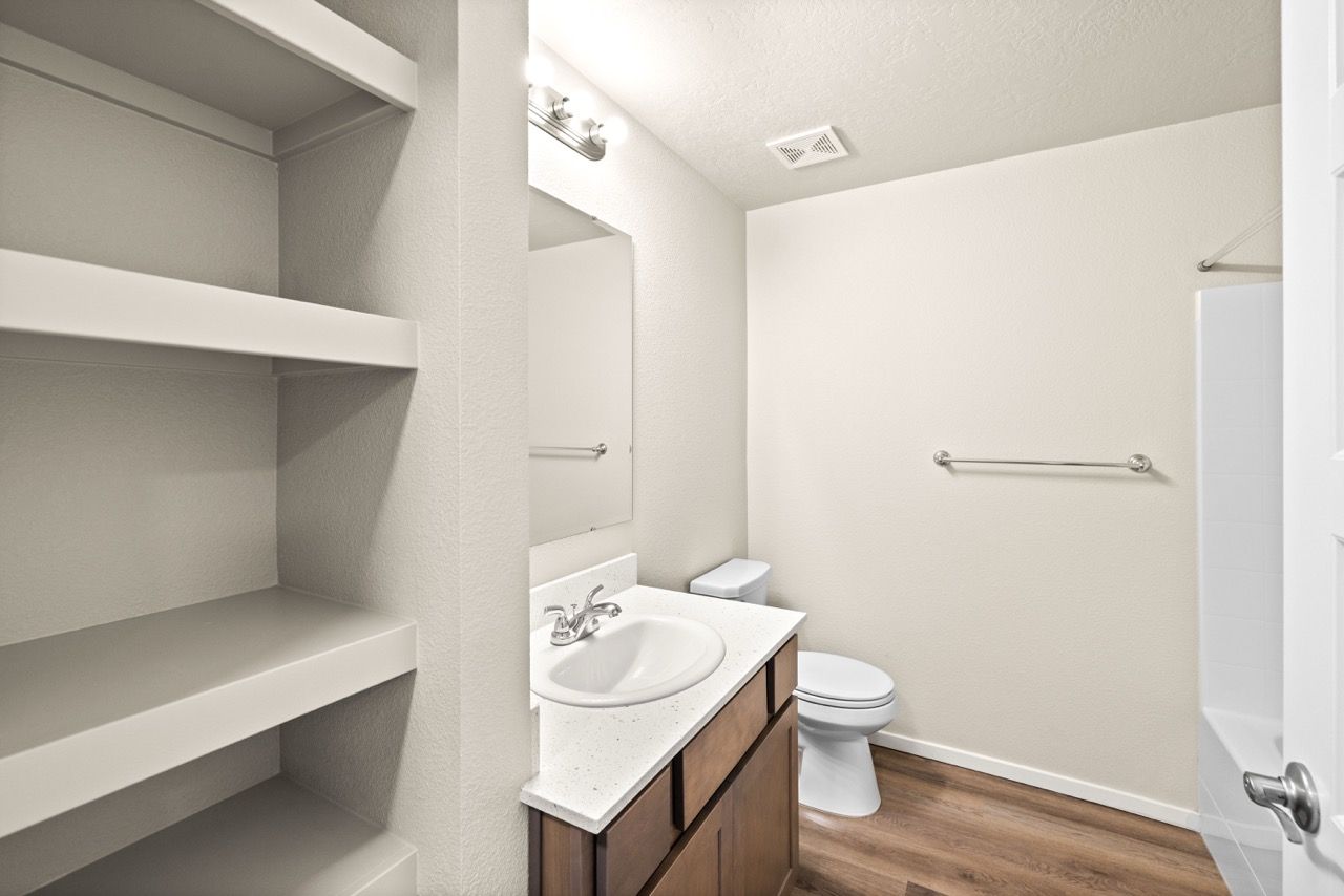 Bathroom in an apartment with vanity, mirror, toilet, tub/shower, and built-in shelves.