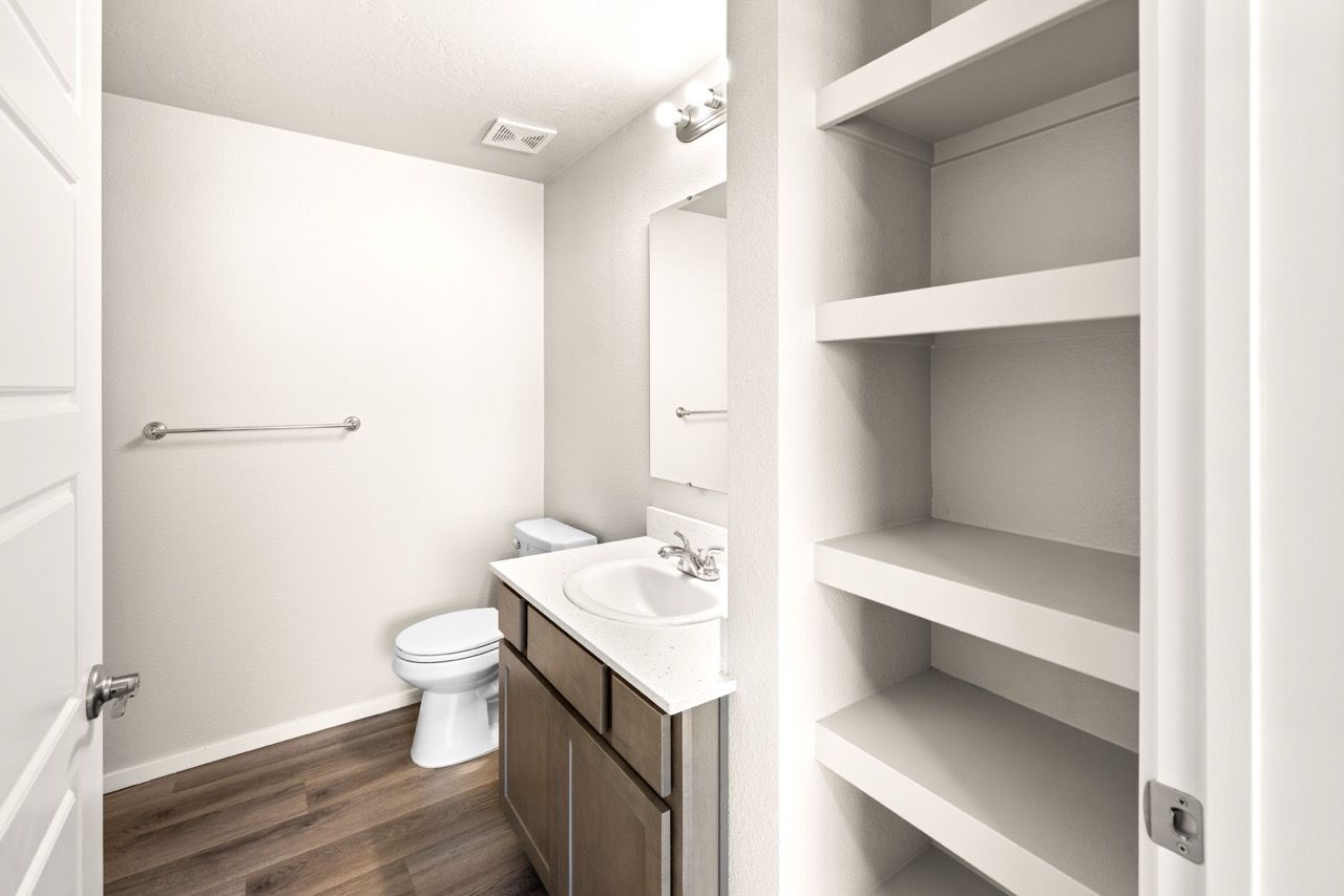 Small apartment bathroom with sink vanity, toilet, mirror, and open shelving.